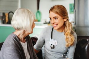 Caring nurse talking with old patient in living room at homecare visit. Medicine caregiving concept