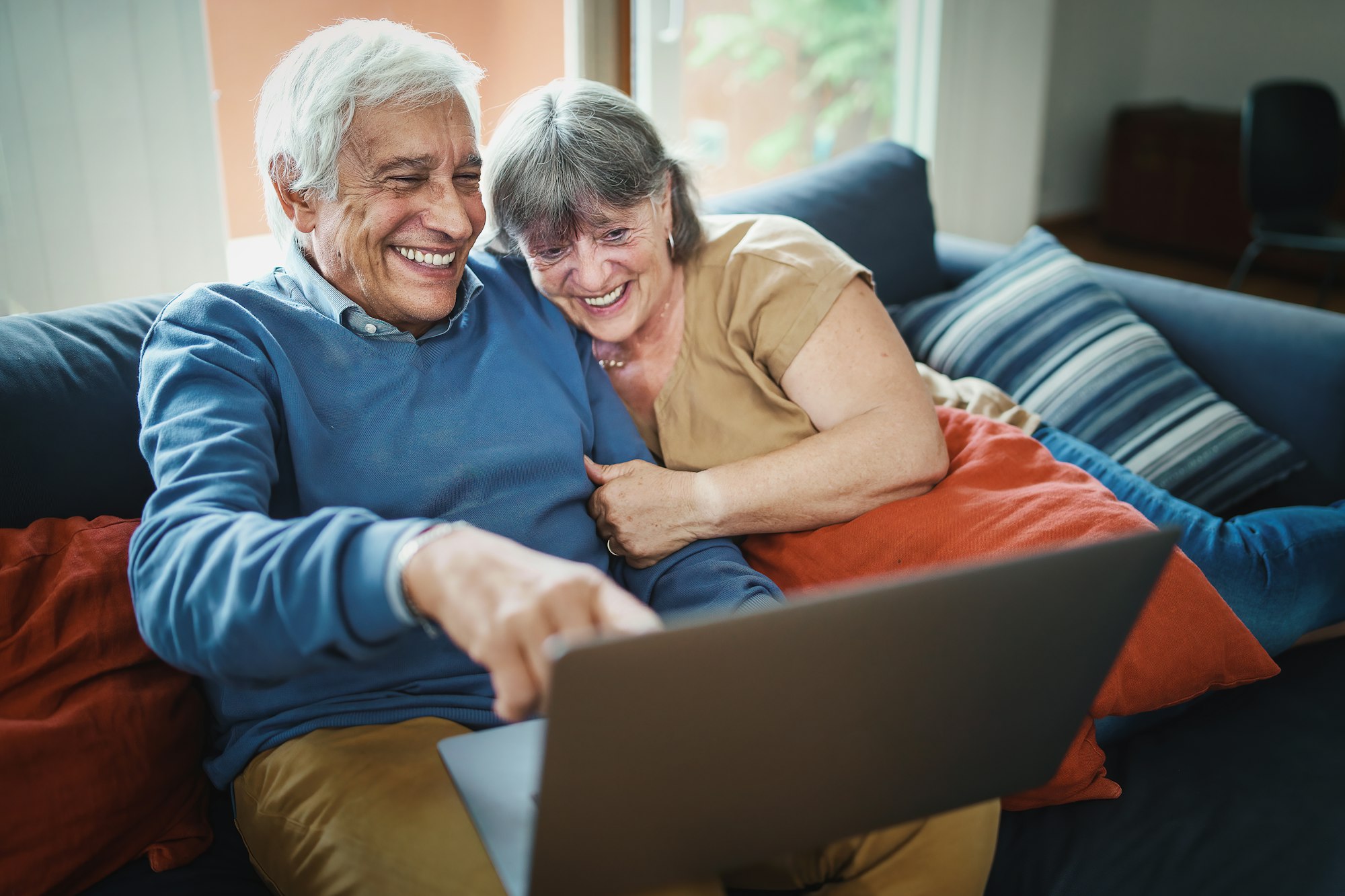 Senior couple watching funny content on a laptop sitting on the couch